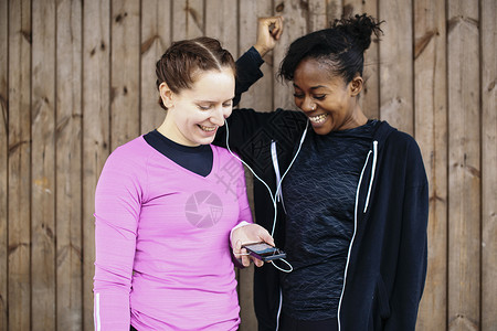 两名在小屋外的年轻妇女分享智能手机音乐图片