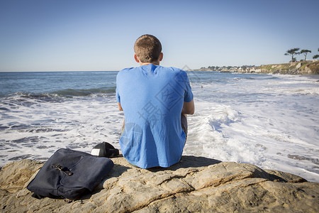 年轻男人坐在岩石旁望向海面后视图片