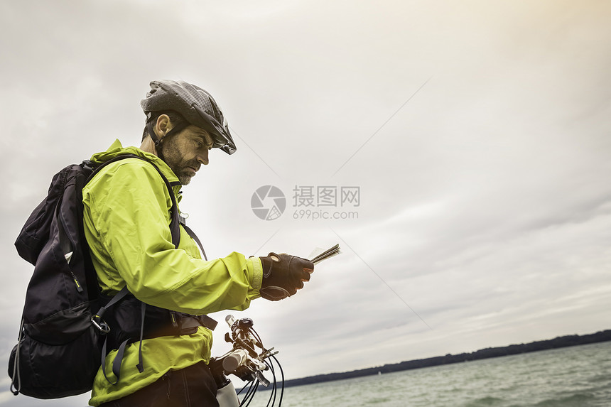 在湖边阅读的男山上骑脚踏车者图片