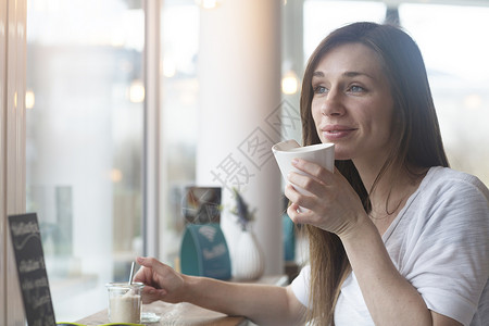 年轻女子透过咖啡店窗口凝视图片