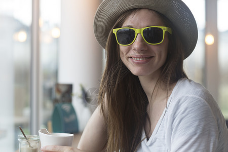 身戴草帽和墨镜的年轻女子在咖啡馆喝图片