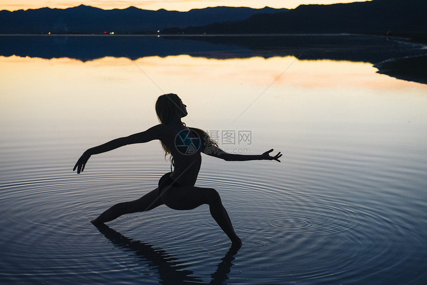 日落时分美国犹他州博纳维尔盐滩湖中一位女舞者的剪影张开双臂图片
