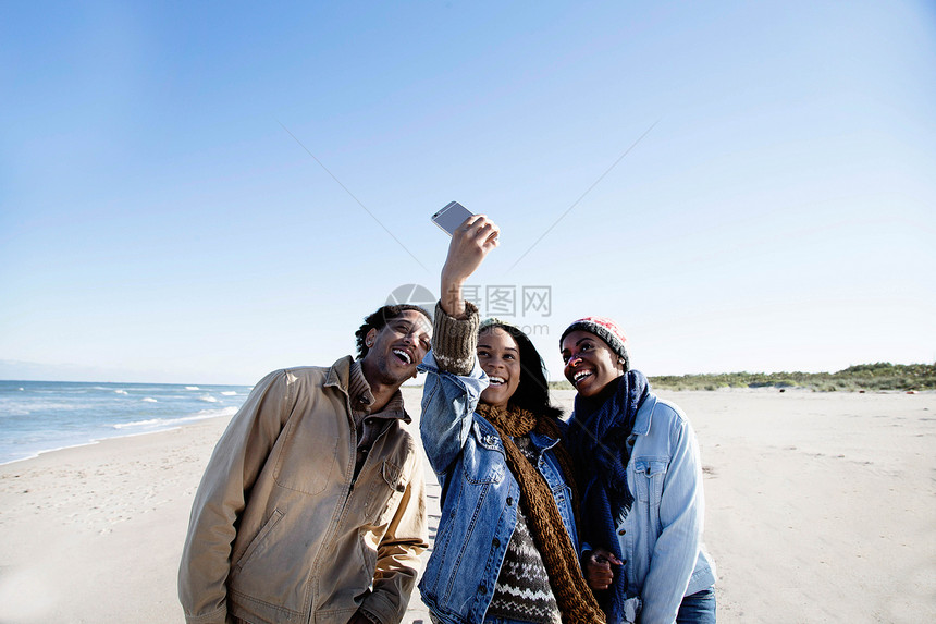 三个朋友在海滩上用智能手机拍自画像图片