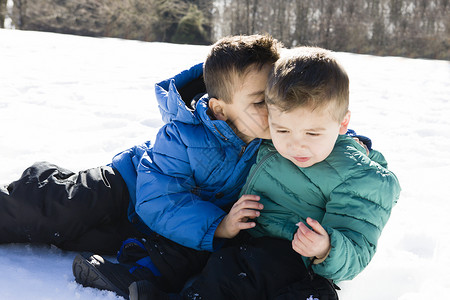 坐在雪上对学龄前男孩低语的兄弟图片