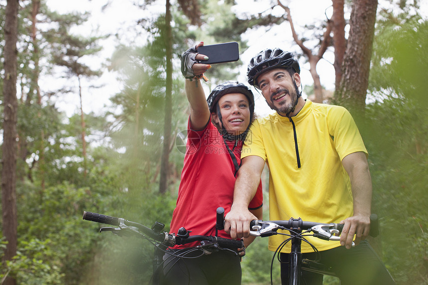 喜的山上骑自行车夫妇假扮在森林里智能手机自拍图片