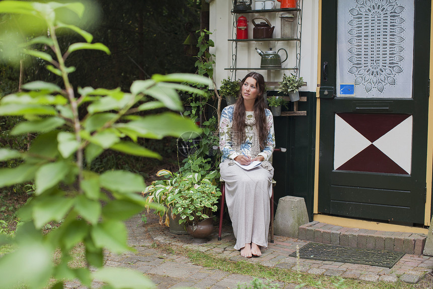 坐在小屋门廊外看边的年轻女子图片