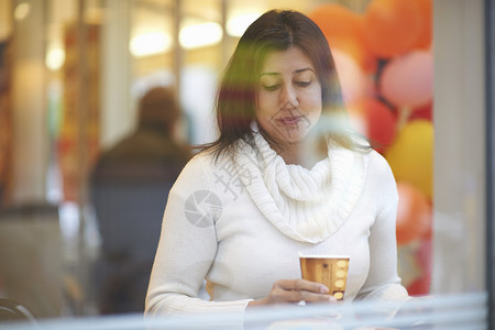 在咖啡厅窗口座位上喝咖啡的成年女性图片