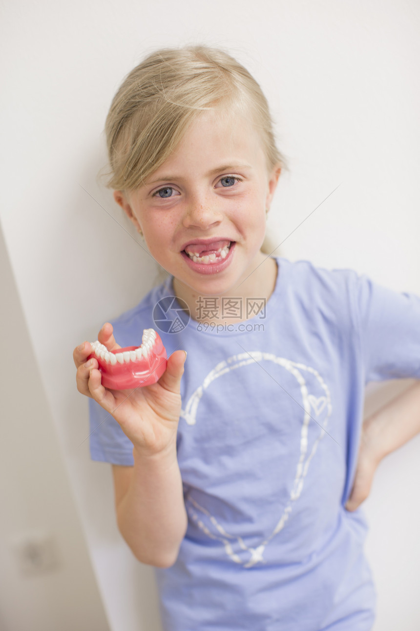 坐在牙医椅子上的女孩拿着假牙微笑图片