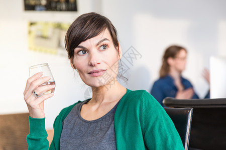 坐在办公室的女性拿着水杯往远处看图片