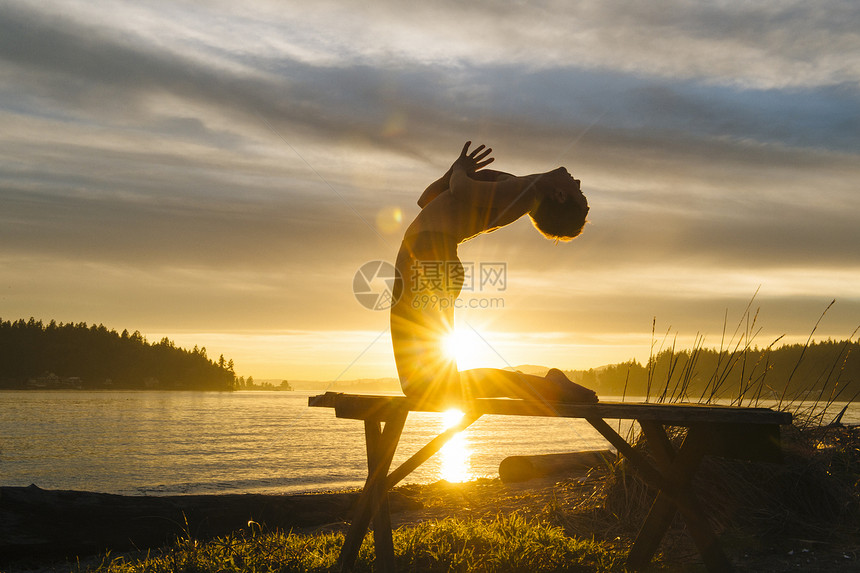 日落时在湖边做瑜伽的妇女图片