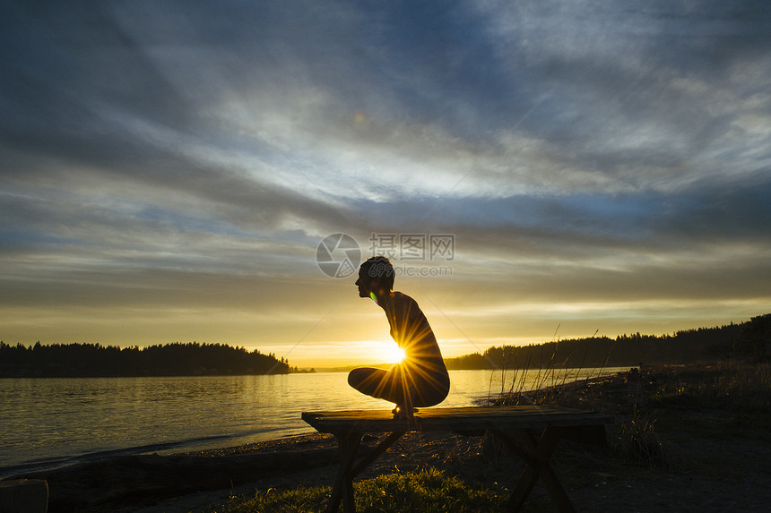 日落时在湖边做瑜伽的女性剪影图片