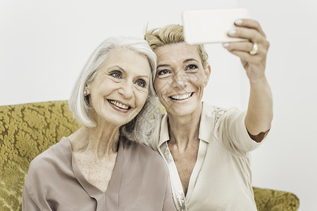 成年母亲和女儿使用智能手机进行自我肖像图片