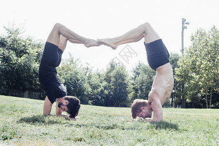 两个男人在公园的瑜伽姿势上颠倒图片