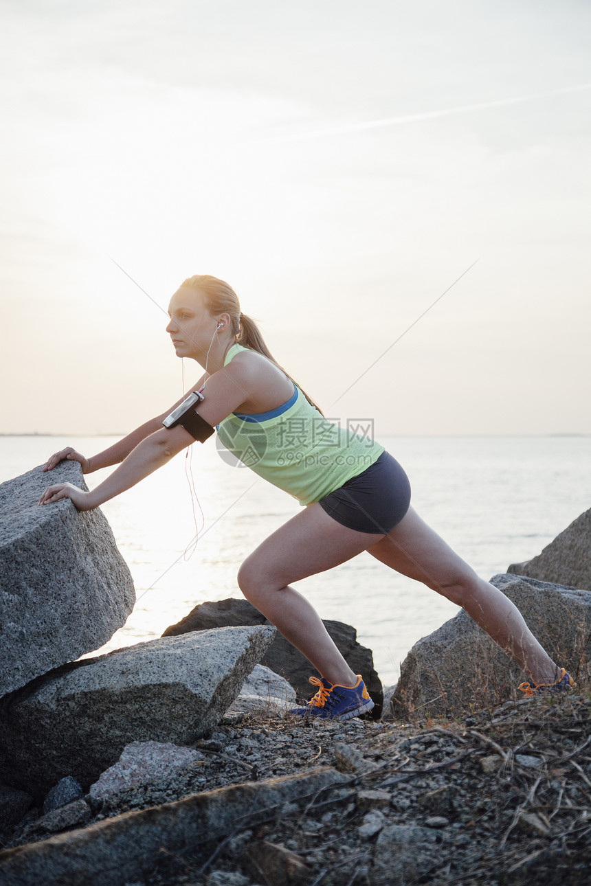 戴着活动跟踪器在岩石上伸展的妇女图片