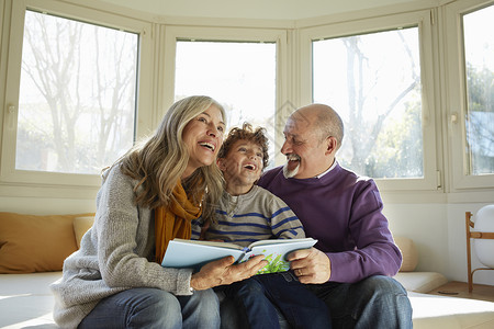 祖父母和孙子一起坐在窗边的椅上笑着看书图片