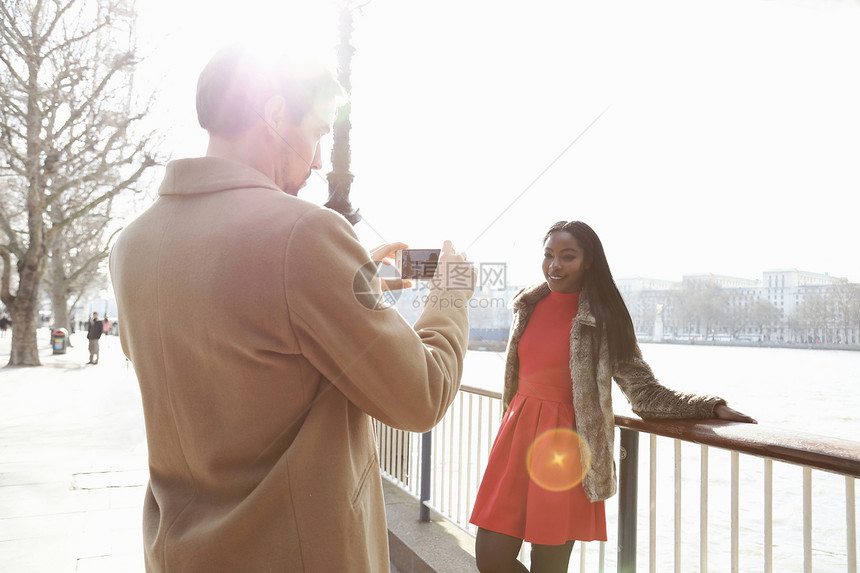 男人给站在河边的年轻女人靠着栏杆拍照片图片