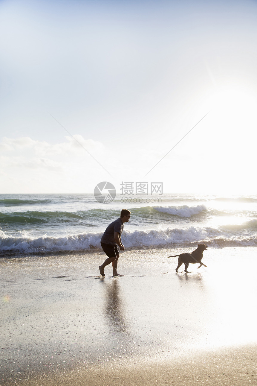 中成年男子和狗在沙滩上玩图片