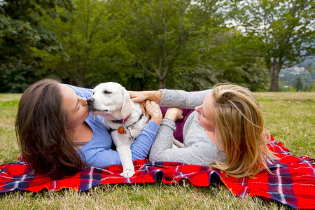 两个带着宠狗的年轻女青躺在公园的毯子上图片