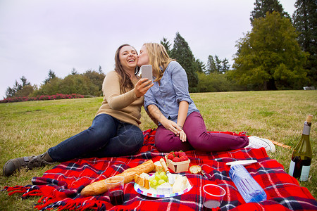两个年轻女子享受公园野餐玩耍自拍用智能手机图片