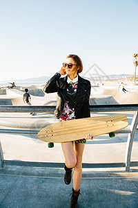 年轻女子站在滑冰公园附近的栏杆旁手持滑板图片