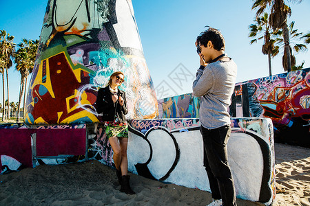 年轻女子站在海滩的涂鸦画艺术旁年轻男子拍她的照片图片