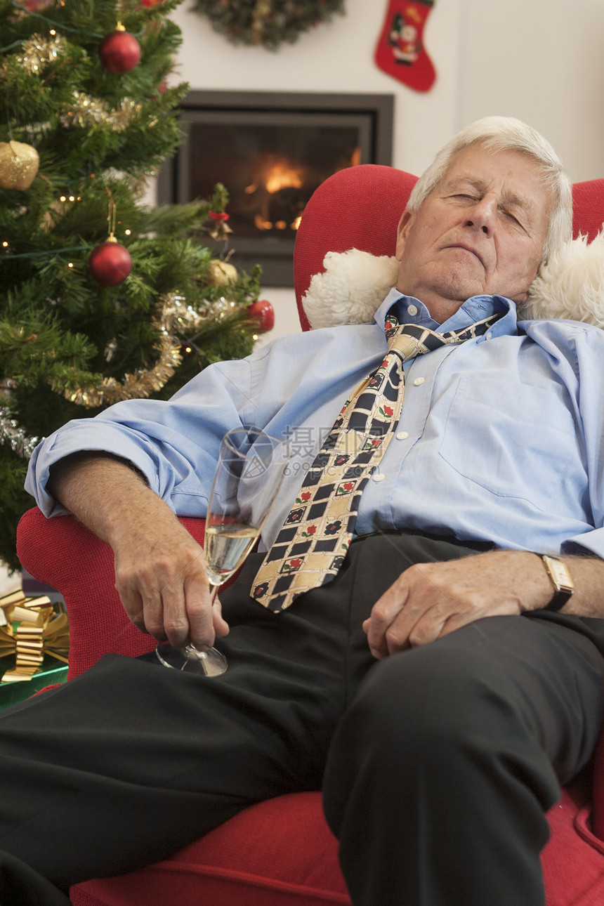 在圣诞节时拿着香槟长笛睡在椅子上的中年男性图片