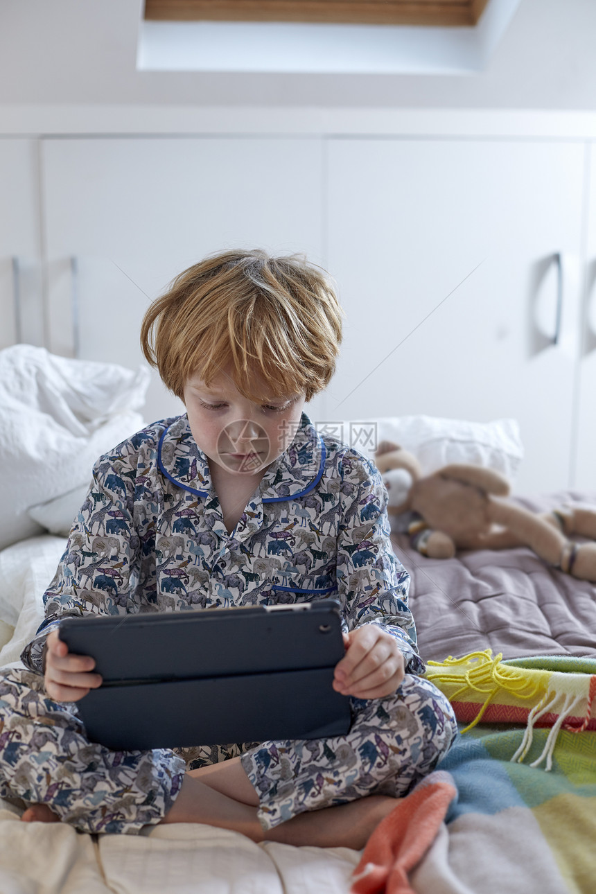 穿睡衣的男孩在床上使用数字平板电脑图片
