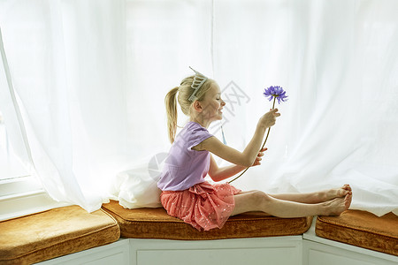 戴发冠头饰的女孩坐在飘窗上拿着一支花的肖像图片