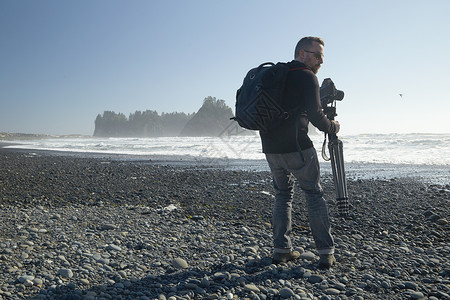 男摄影师在海滩上携带相机和三脚架高清图片