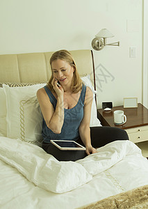 坐在床上使用手机打电话的年轻女性图片