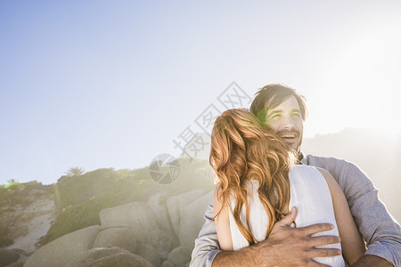 在岩石前男人拥抱女人微笑背景图片