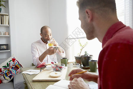 坐在饭桌上喝橙汁看着智能手机的青年男性图片