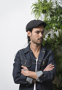 穿着平顶帽站在叶墙前的年轻男潮人肖像图片