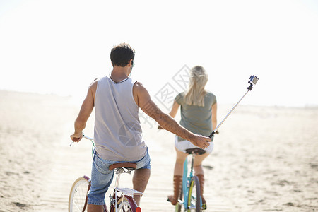 在海滩骑自行车用自拍杆拍照的情侣背影图片