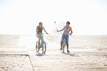 在海滩骑自行车用自拍杆拍照的情侣图片