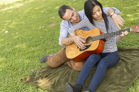坐在草地上教女人弹声吉他的男图片