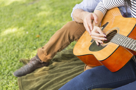 一对坐在草地上弹声吉他的小夫妻切成景象图片