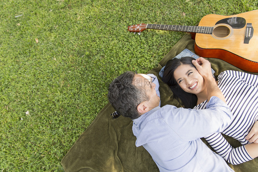 从高角度看一对躺在草地上带着声响吉他微笑的情侣图片