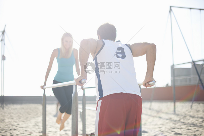一对夫妇在海滩上运动使用平行的体操酒吧图片