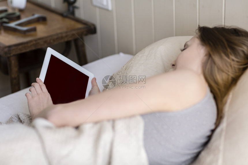 年轻女性躺在床上使用平板电脑图片