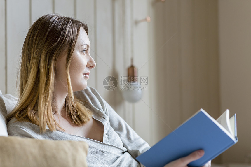 坐在床上拿着书看向远方的年轻女性图片