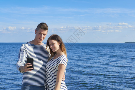 年轻夫妇在海上站立使用智能手机合照图片