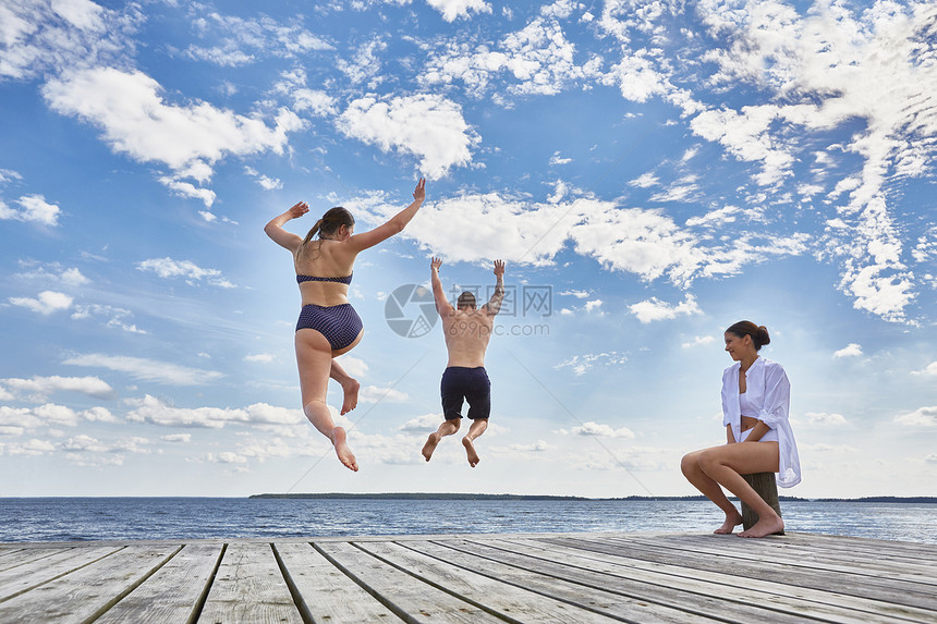 坐在木码头上的年轻女士看着朋友跳进海里玩耍图片