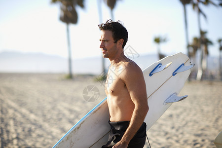 夹着冲浪板在沙滩上的男人图片