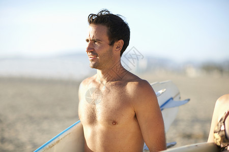 夹着冲浪板在沙滩上的男人图片