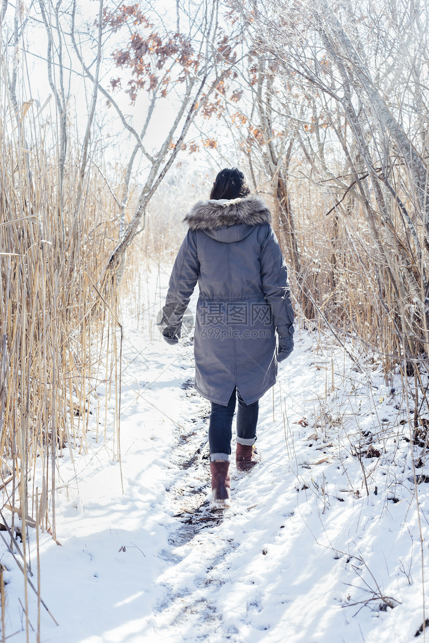 身穿冬大衣在雪地上行走的妇女的背影图片