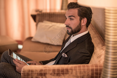 迪拜冲沙青年商人坐在旅馆沙发上使用数字平板电脑背景