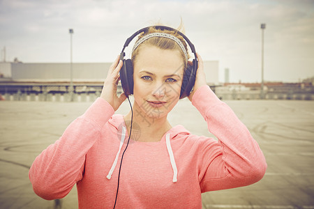 女人用手摸着耳机在屋顶停车场听音乐图片
