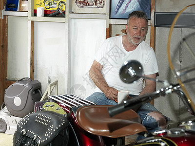 坐在车库的摩托上拿着咖啡的老人图片