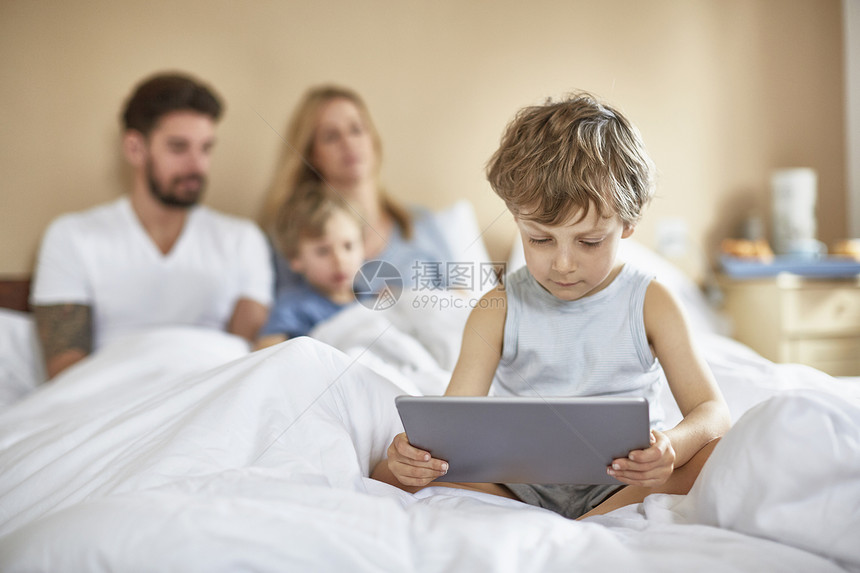 使用数字平板电脑在父母床上睡觉的男孩图片